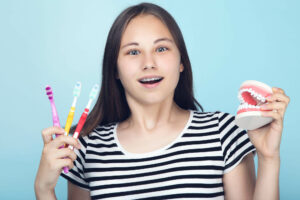 teen girl with braces holding a fake mouth and toothbrushes