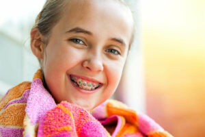 cute girl smiling with braces while wrapped up in a towel after swimming